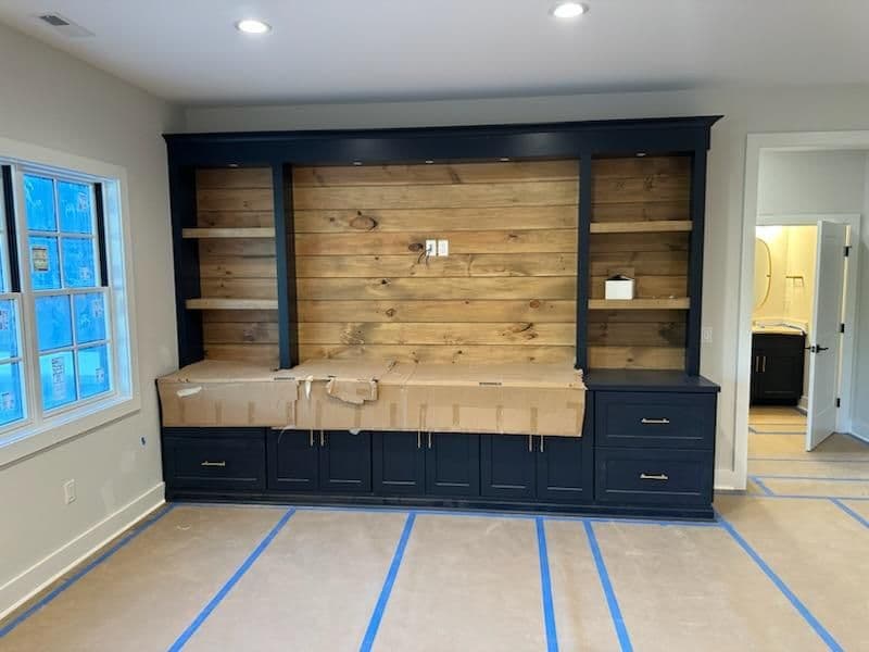 Modern navy blue built-in cabinetry with wooden shelves, under construction in a bright room.