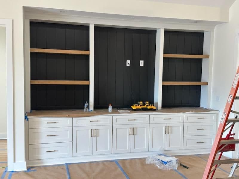 Modern white cabinet with dark wooden shelves, under construction, in a home interior.