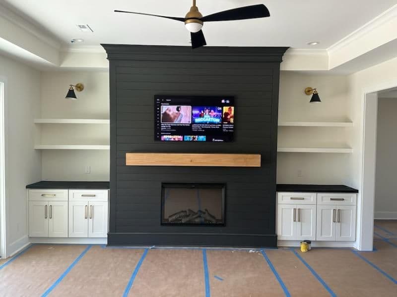 Modern living room with black feature wall, TV, wooden mantel, and white cabinetry.