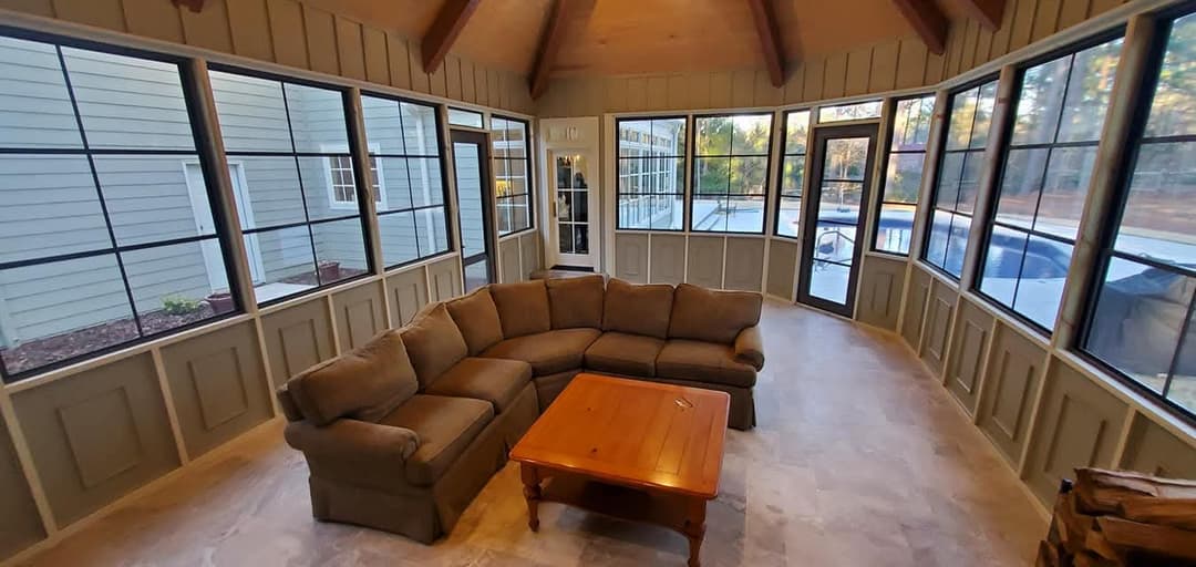Spacious sunroom with large windows, a cozy sectional sofa, and wooden coffee table.