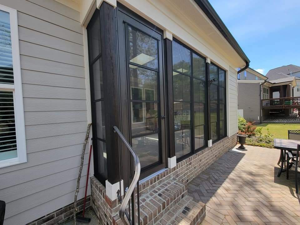 Modern sunroom addition with large windows and brick patio beside a residential home.