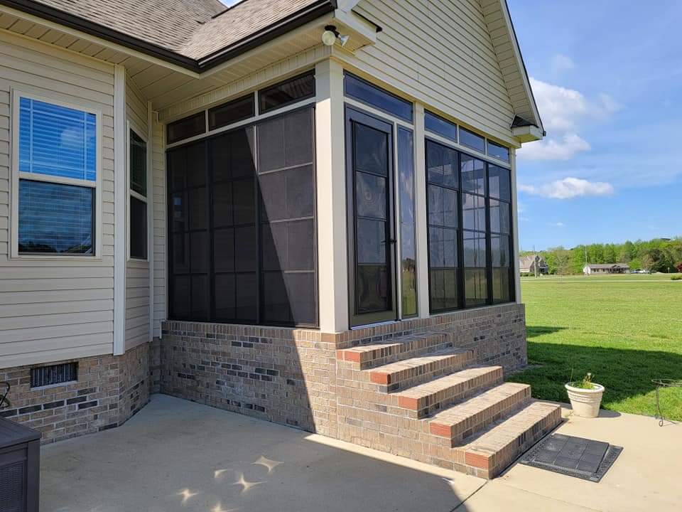 Screened porch addition on a house with brick stairs and a green lawn backdrop.