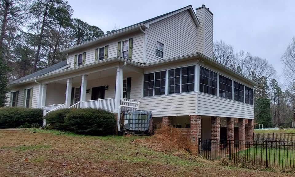Two-story white house with screened porch, surrounded by green lawn and trees.