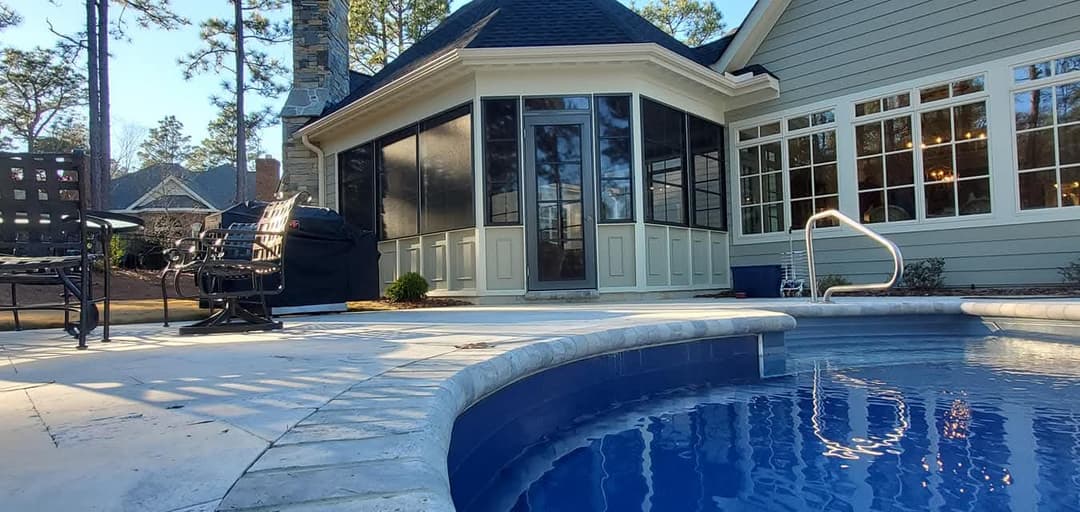 Modern backyard patio with pool, screened porch, and cozy seating area surrounded by trees.