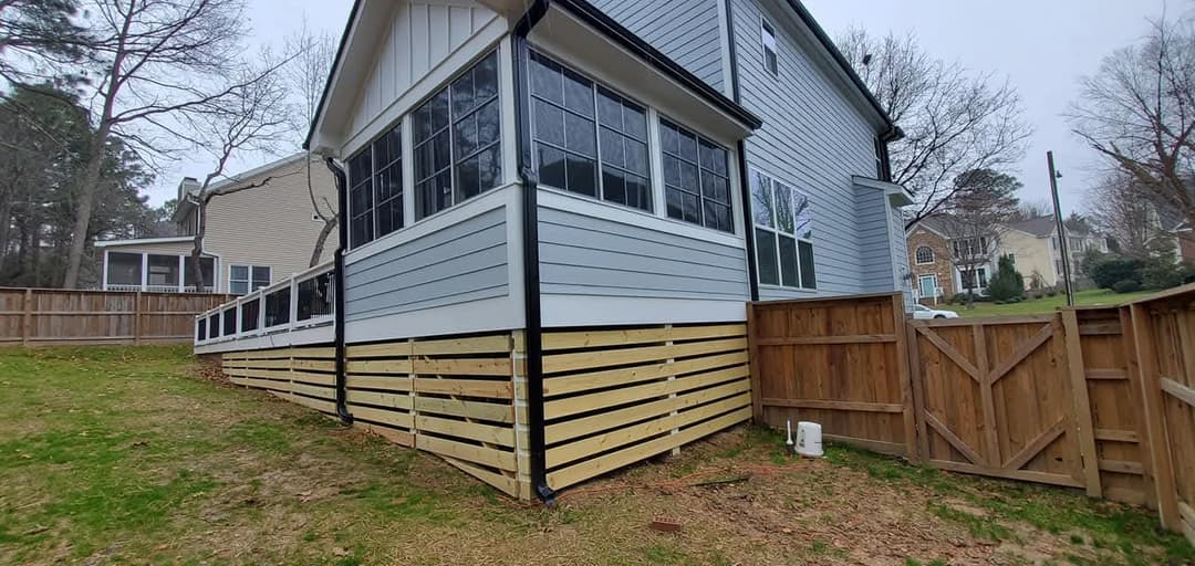 Modern home exterior with a screened porch, wooden skirting, and fenced yard.