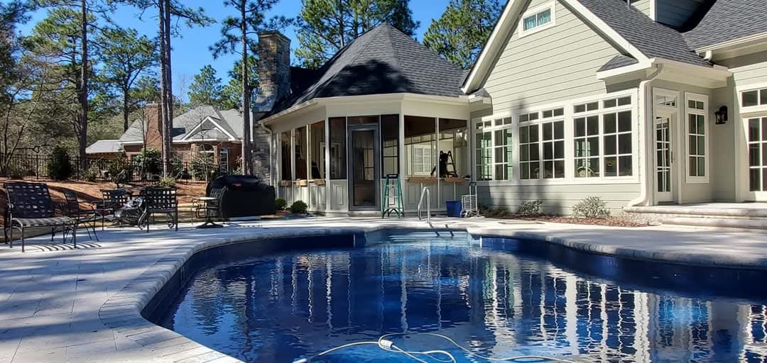 Luxury home with a blue pool, outdoor seating, and a landscaped backyard in a wooded area.