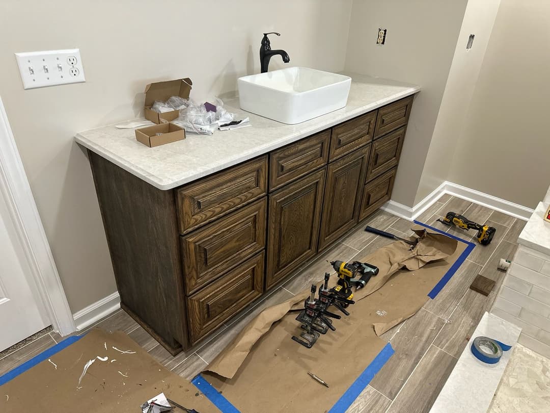 Modern bathroom vanity installation with sink, wood cabinetry, and tools on the floor.