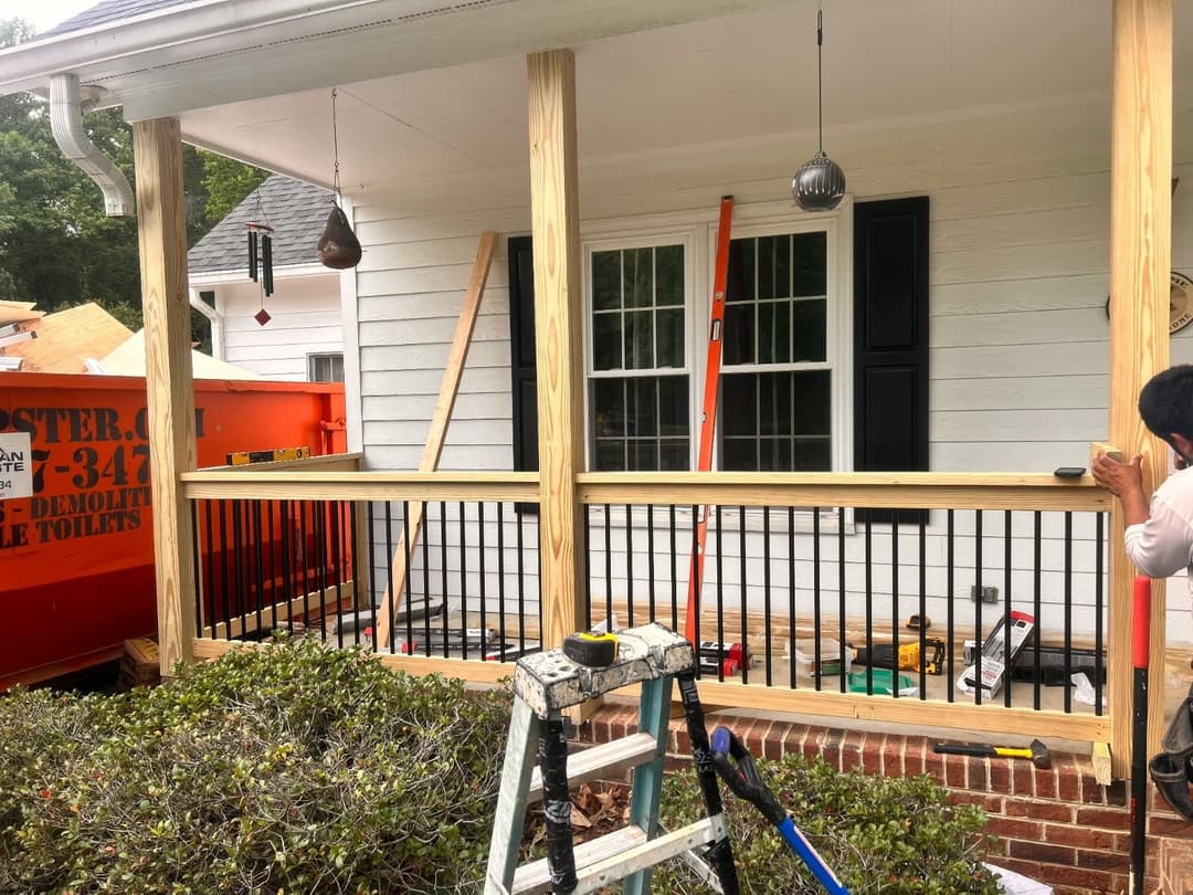 Construction of a new porch railing with wooden posts and black metal balusters.