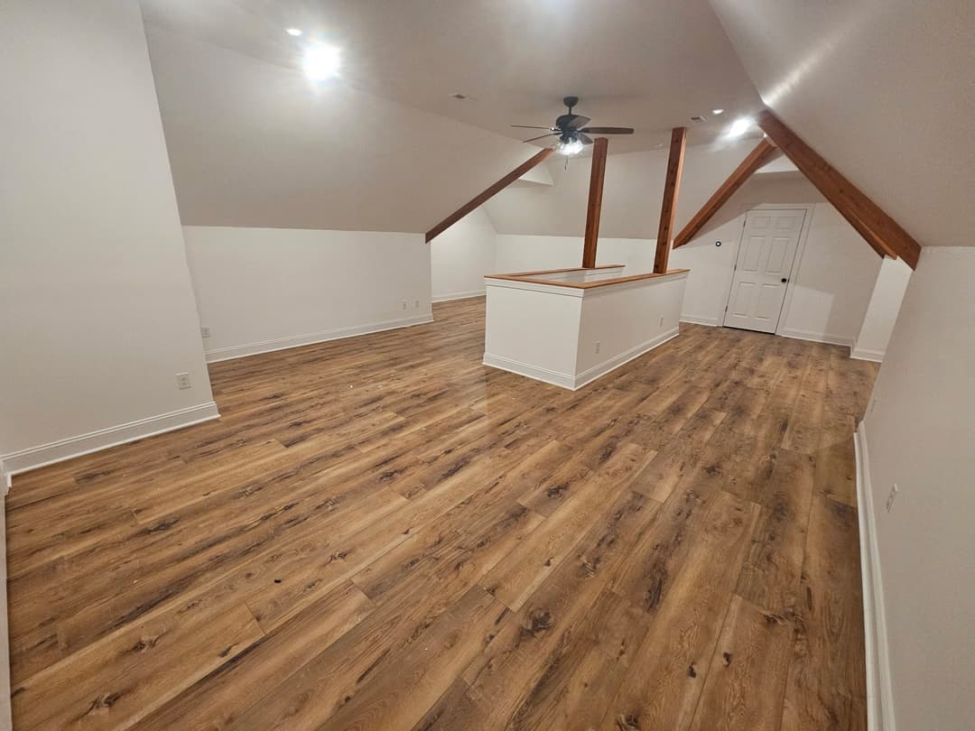 Spacious, well-lit loft with wooden floors and exposed beams, featuring a ceiling fan.