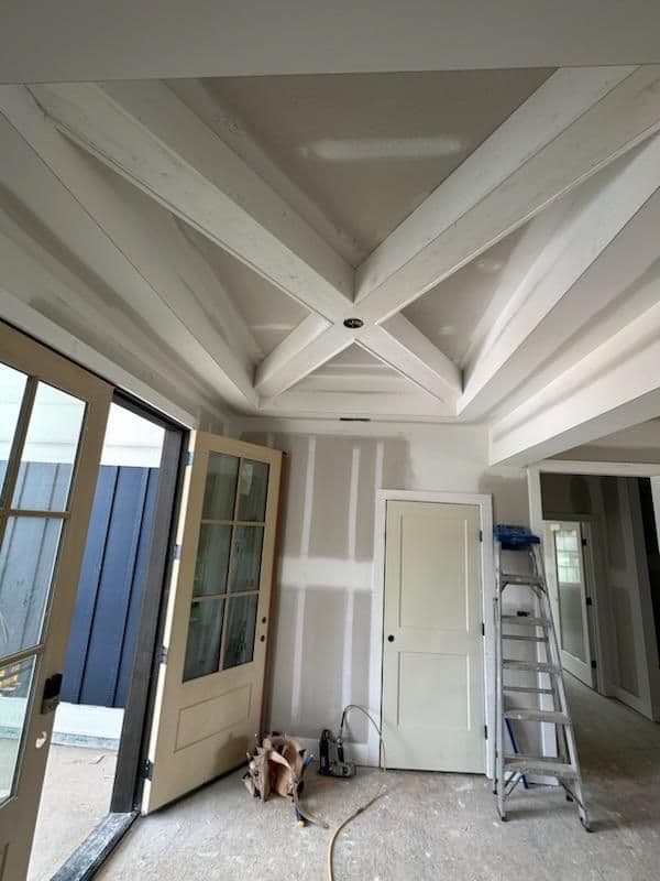 Newly renovated room showcasing a coffered ceiling and unfinished drywall with open doors.