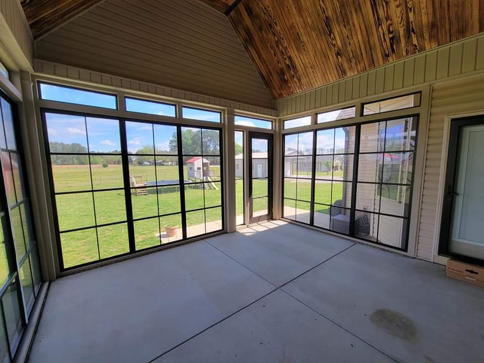Spacious screened-in porch with wooden ceiling and views of green yard and outdoor buildings.