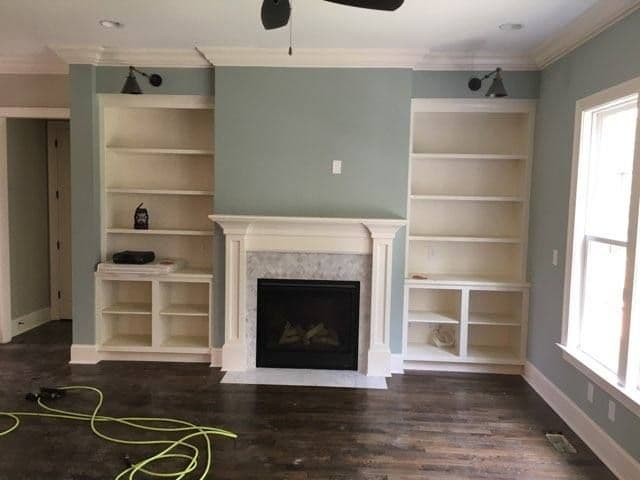 Living room with built-in shelves and a fireplace, featuring light green walls and dark wood flooring.