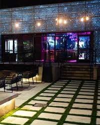 Nighttime outdoor dining area with modern decor, illuminated pathway, and twinkling lights.