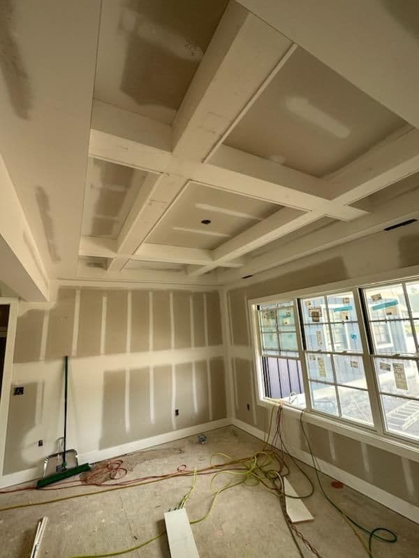 Modern room with coffered ceiling under construction, featuring windows and drywall work.