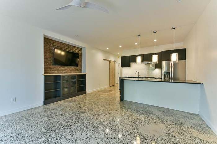 Modern kitchen and living area with exposed brick, pendant lights, and polished concrete floor.