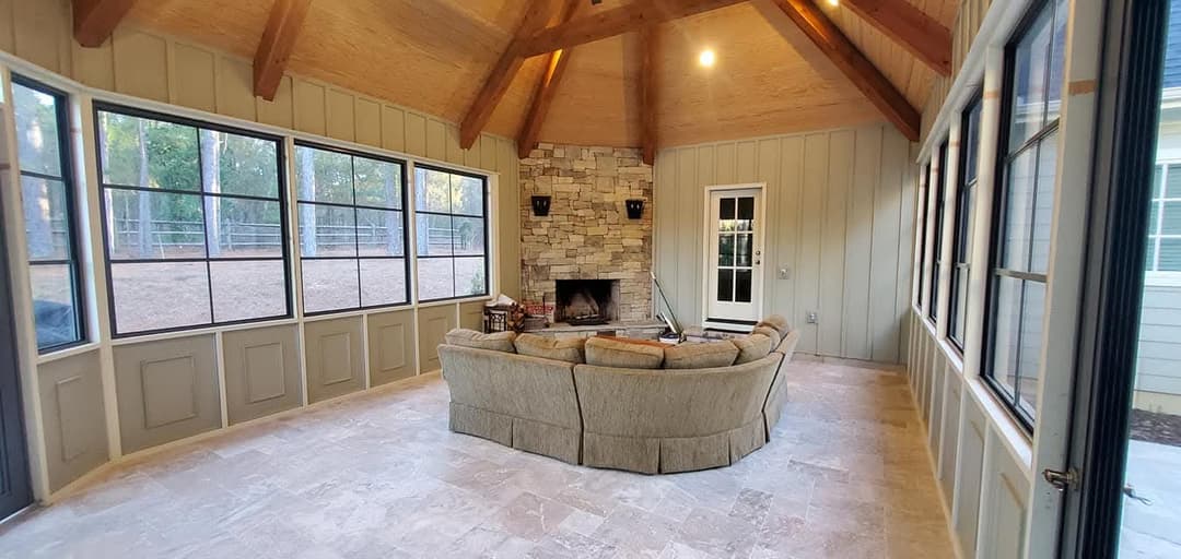 Cozy sunroom with stone fireplace, wooden beams, and comfortable seating for relaxation.