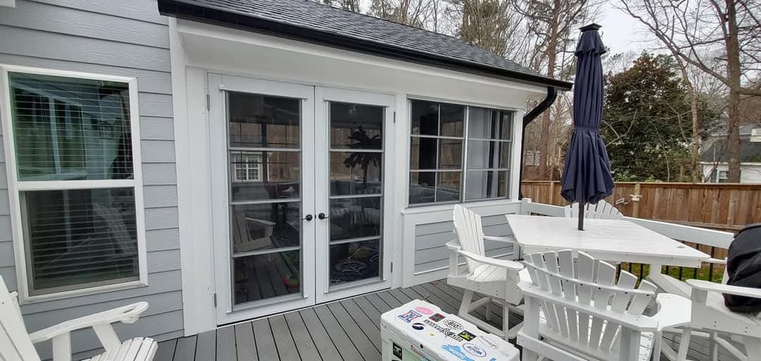 Bright sunroom with sliding glass doors, white outdoor furniture, and a cozy deck area.