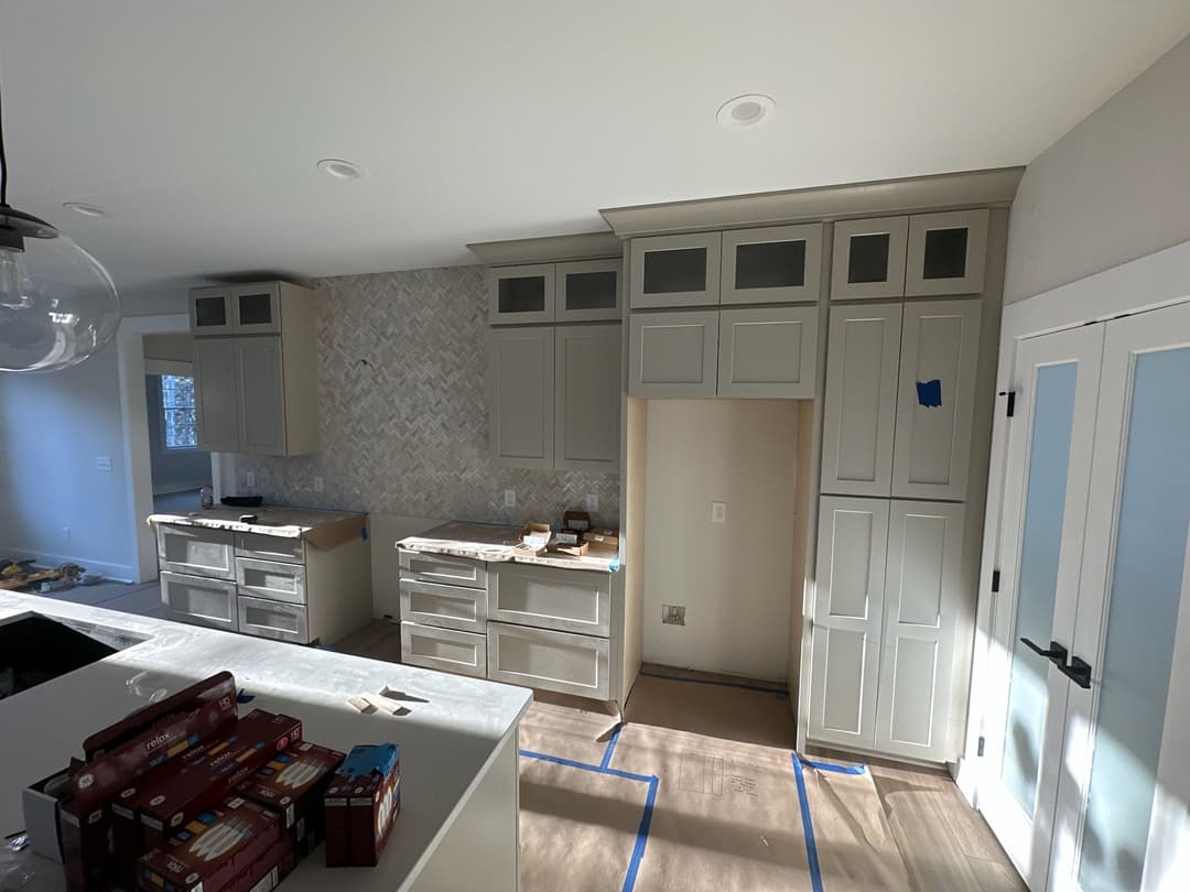 Modern kitchen with light gray cabinets, herringbone backsplash, and under-construction elements.