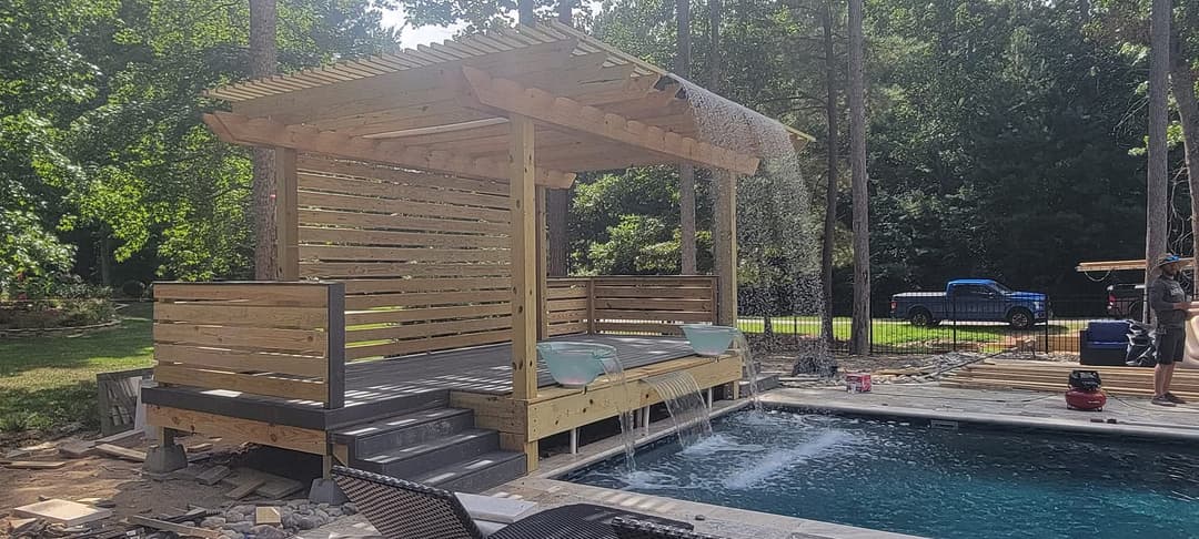Wooden pavilion with two bathtubs beside a swimming pool in a lush backyard setting.