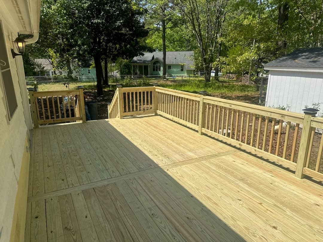 Spacious wooden deck in a sunny backyard surrounded by trees and houses.