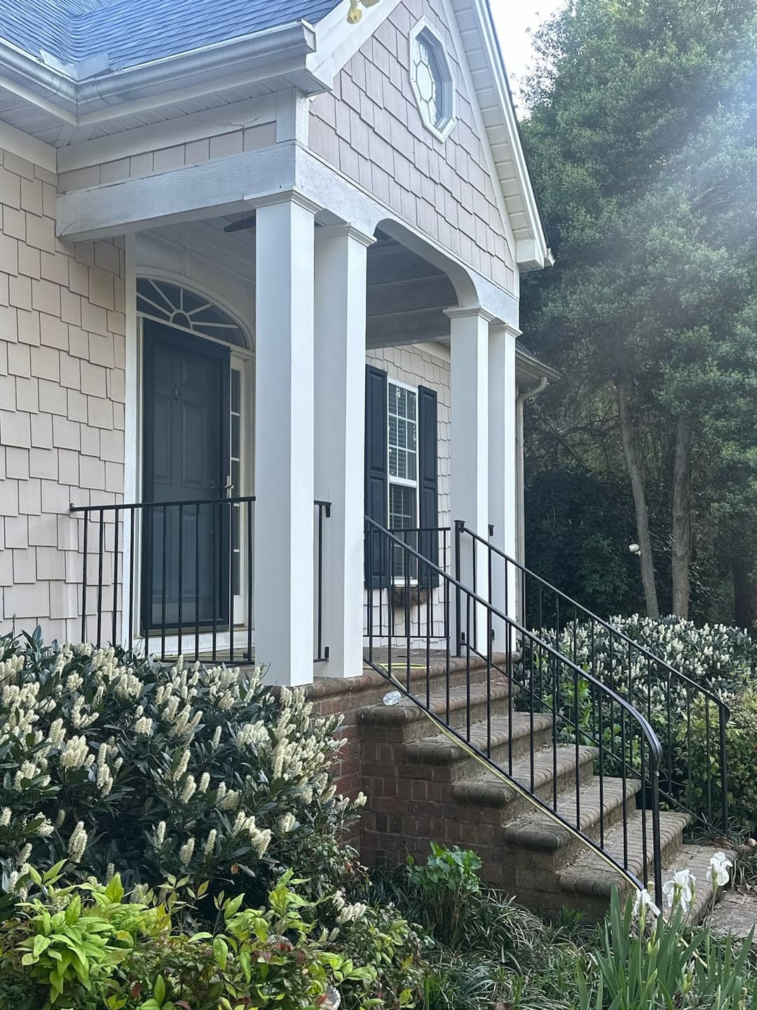 Charming house entrance with stairs, white columns, and lush garden landscaping.