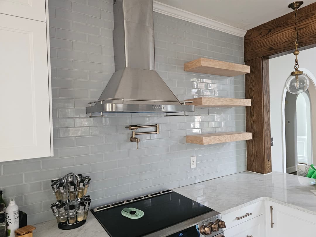 Modern kitchen with stainless steel range hood, open wooden shelves, and marble countertop.