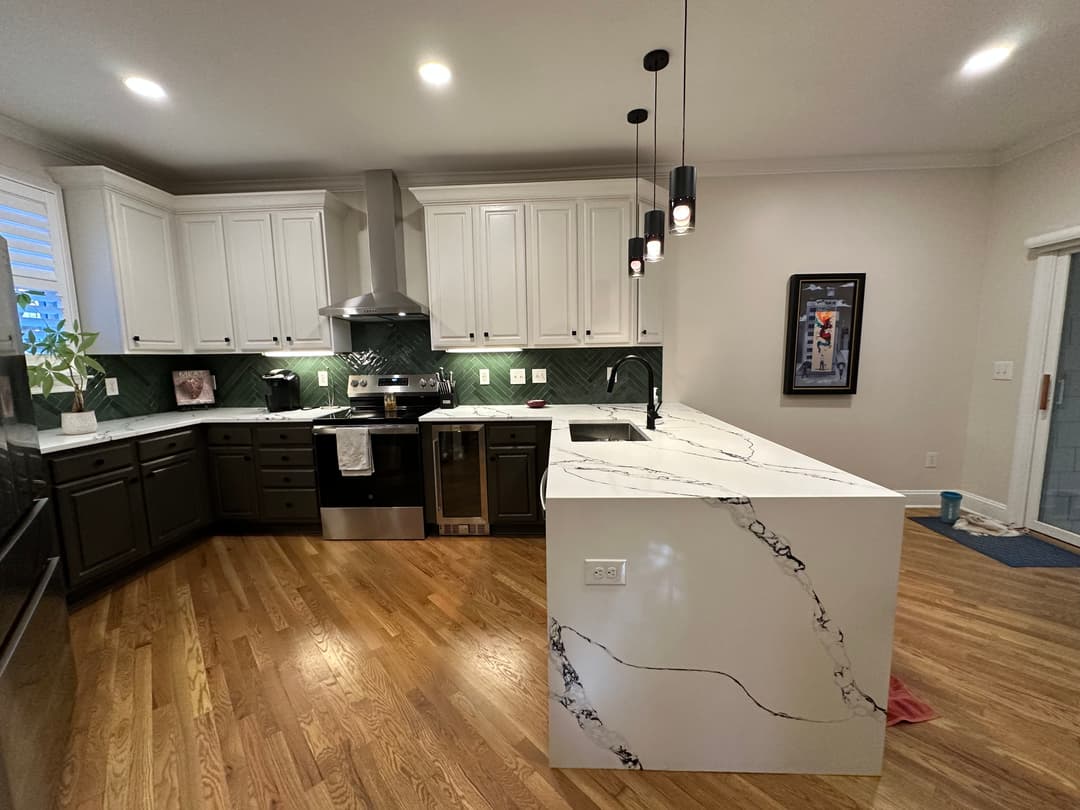 Modern kitchen with marble island, dark cabinets, and stainless steel appliances.