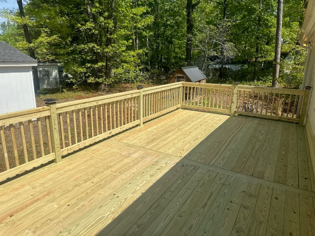 New wooden deck in a wooded area, featuring railings and sunlight filtering through trees.