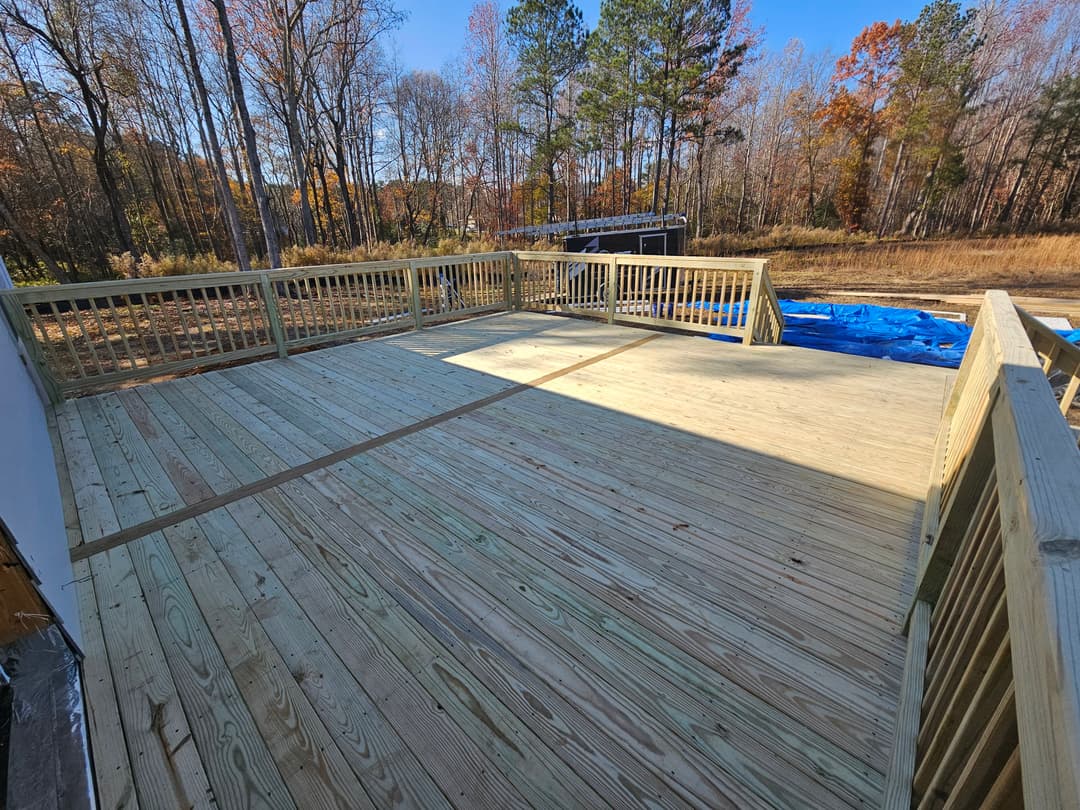 Newly built wooden deck surrounded by trees in autumn, featuring railings and sunlight.