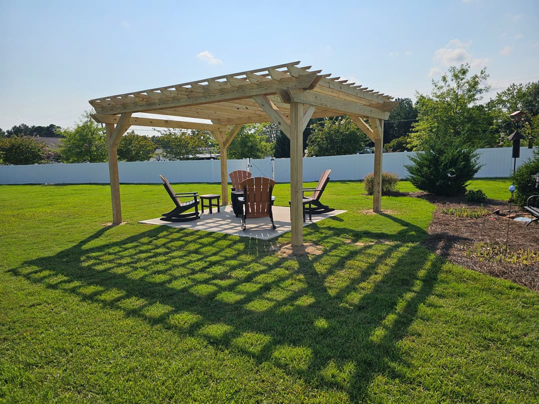 Wooden pergola with Adirondack chairs casting shadows on a lush green lawn.