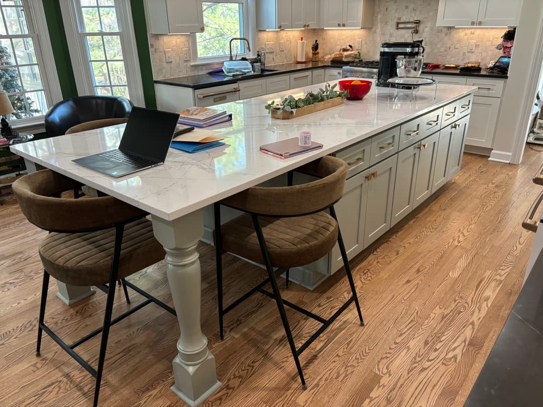 Modern kitchen with marble island, bar stools, laptop, and a cozy, bright atmosphere.
