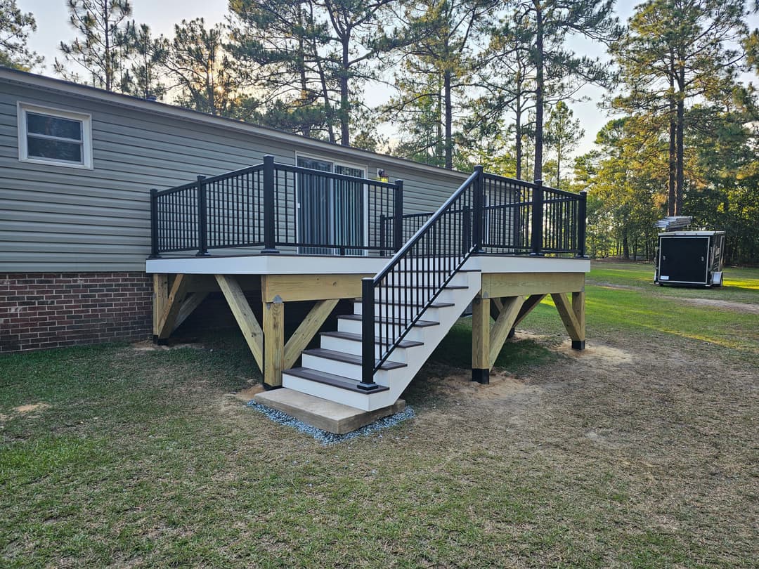 Modern deck with black railing and stairs, surrounded by trees and grass.