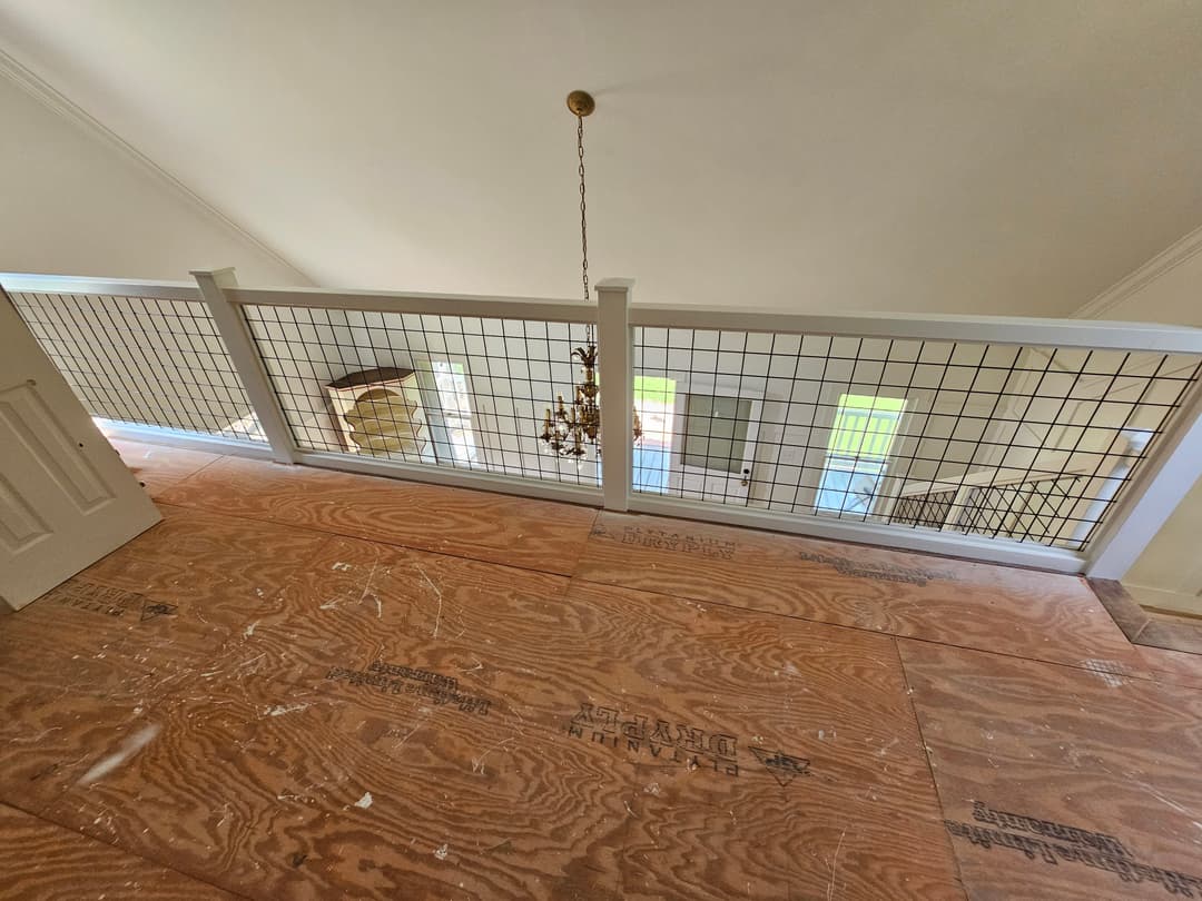 View of unfinished upstairs hall with wooden flooring, metal railing, and chandelier.