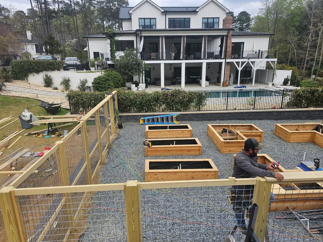 Construction site with wooden garden beds, landscaping, and modern house in background.