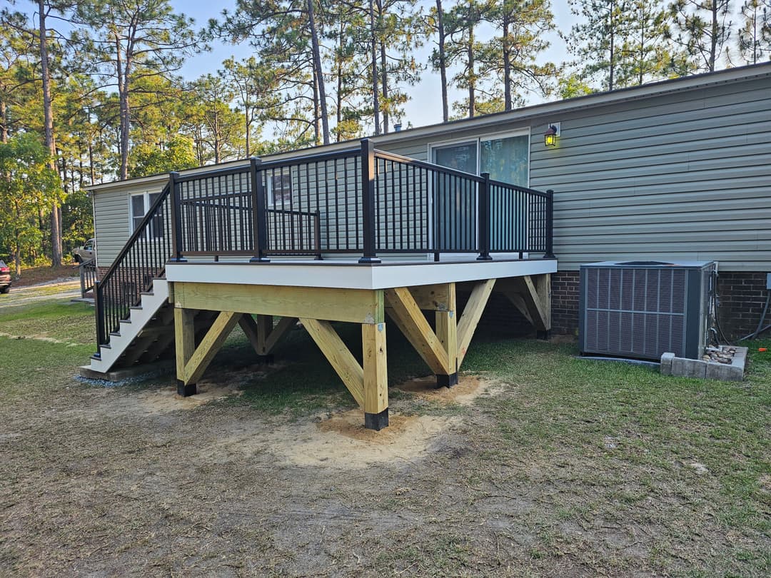 Updated outdoor deck with black railings, stairs, and air conditioning unit beside a home.