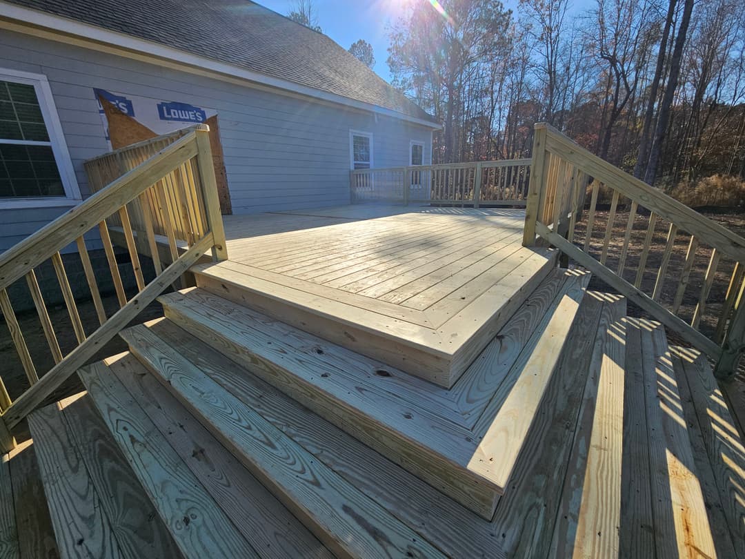 Newly built wooden deck with steps on a sunny day, showcasing craftsmanship and design.