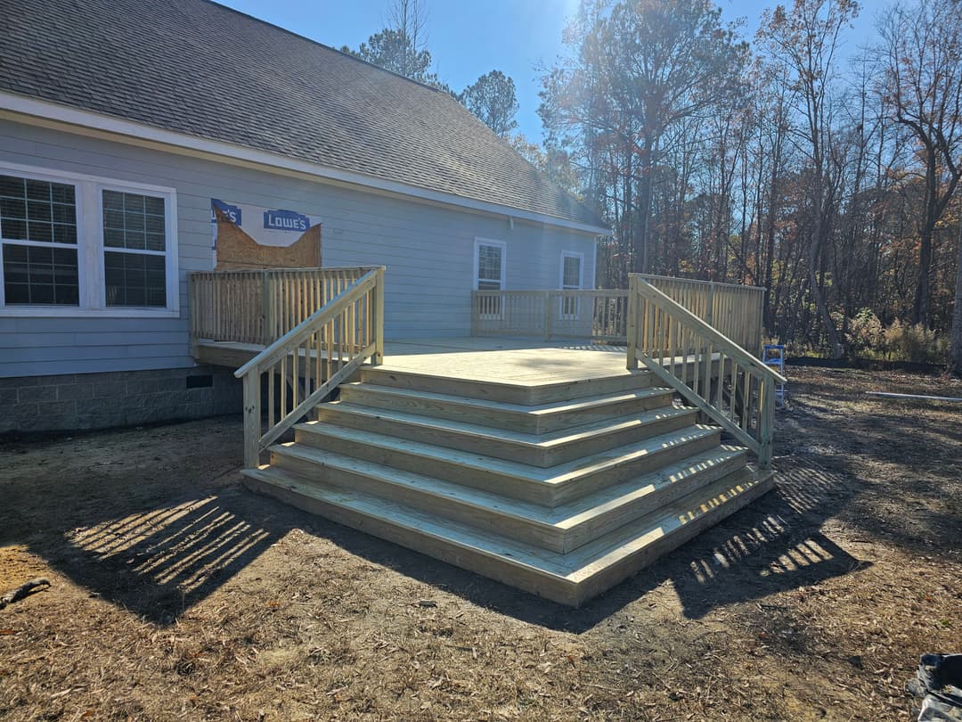 Newly built wooden deck with railings, featuring multiple steps, beside a house surrounded by trees.