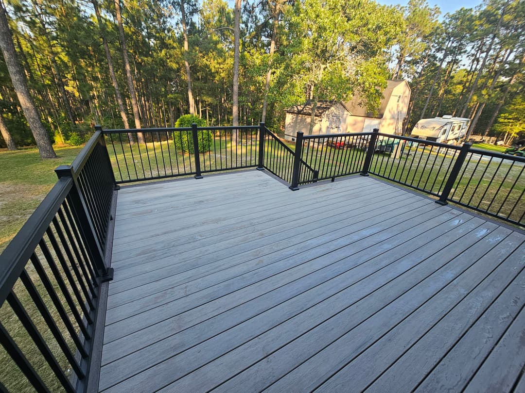 Spacious deck overlooking trees and a home, featuring black railings and a sunny atmosphere.