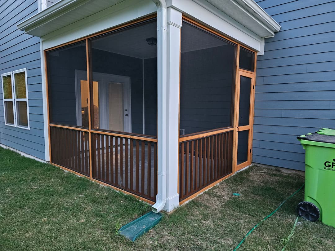 Screened porch addition with wooden framing on a modern home exterior. Green trash bin nearby.