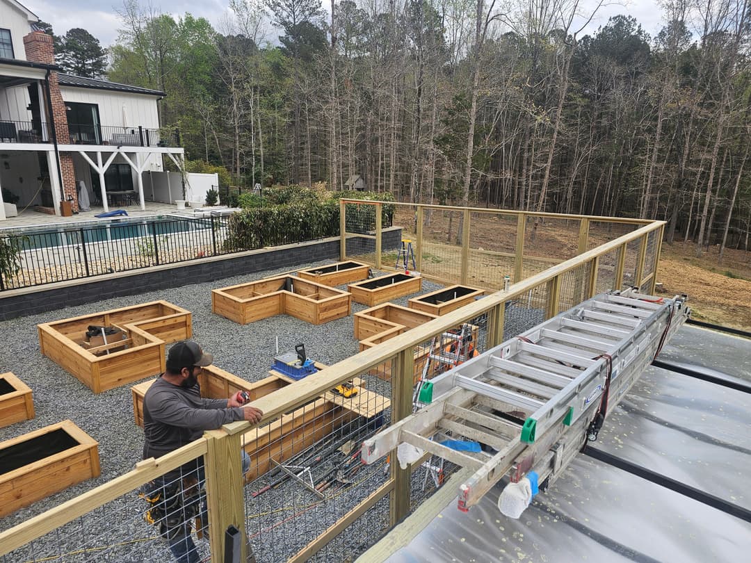 Wooden garden beds under construction in a backyard with a ladder and house in the background.