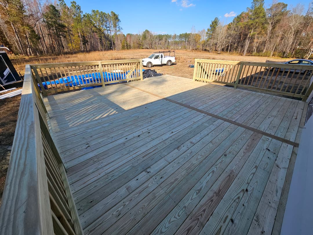 Newly built wooden deck overlooking a grassy field and wooded area, with a truck in the background.
